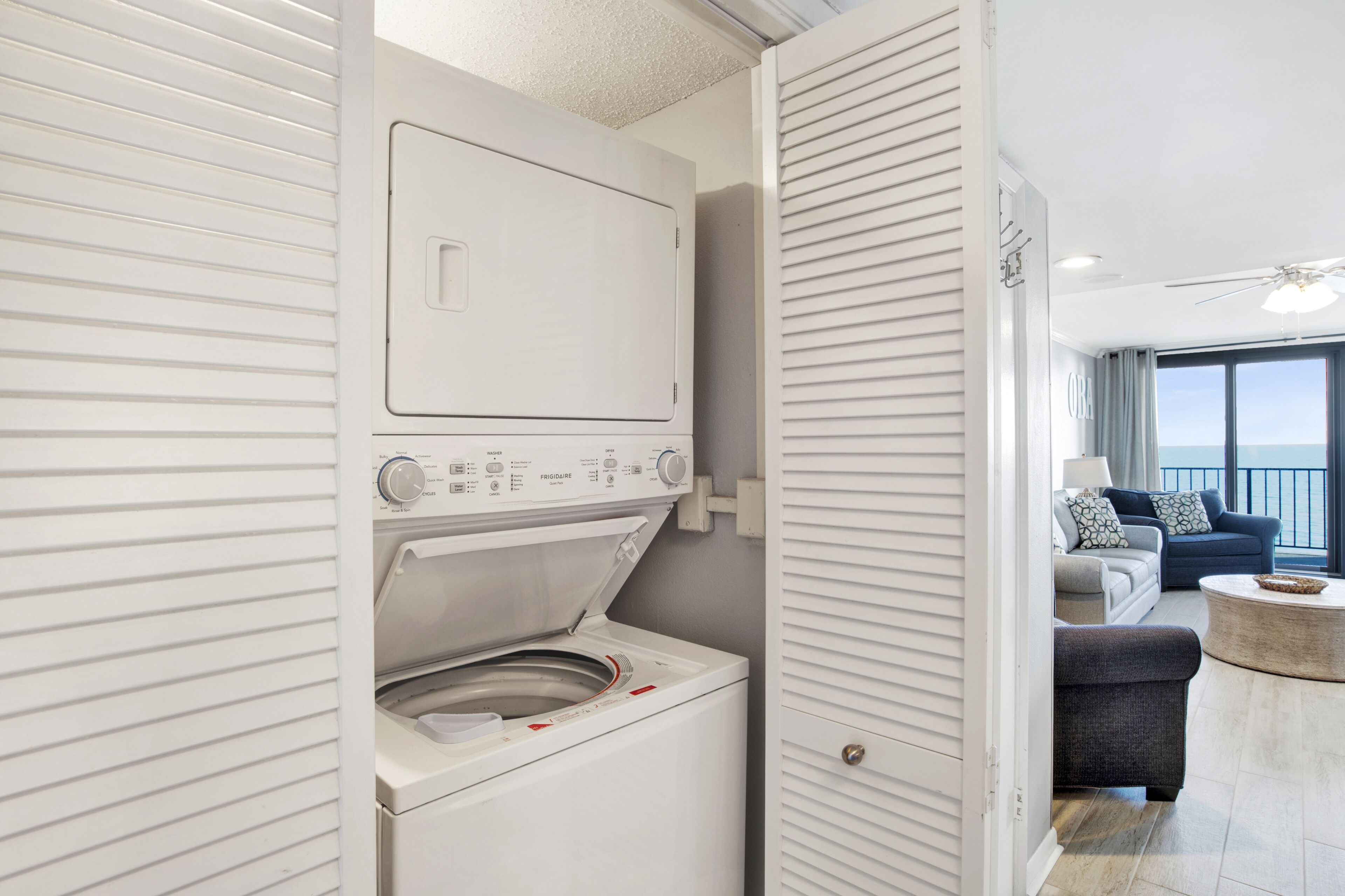 A laundry room with a front-loading washer and dryer, a sliding door leading to a living area with a sofa and a round coffee table.