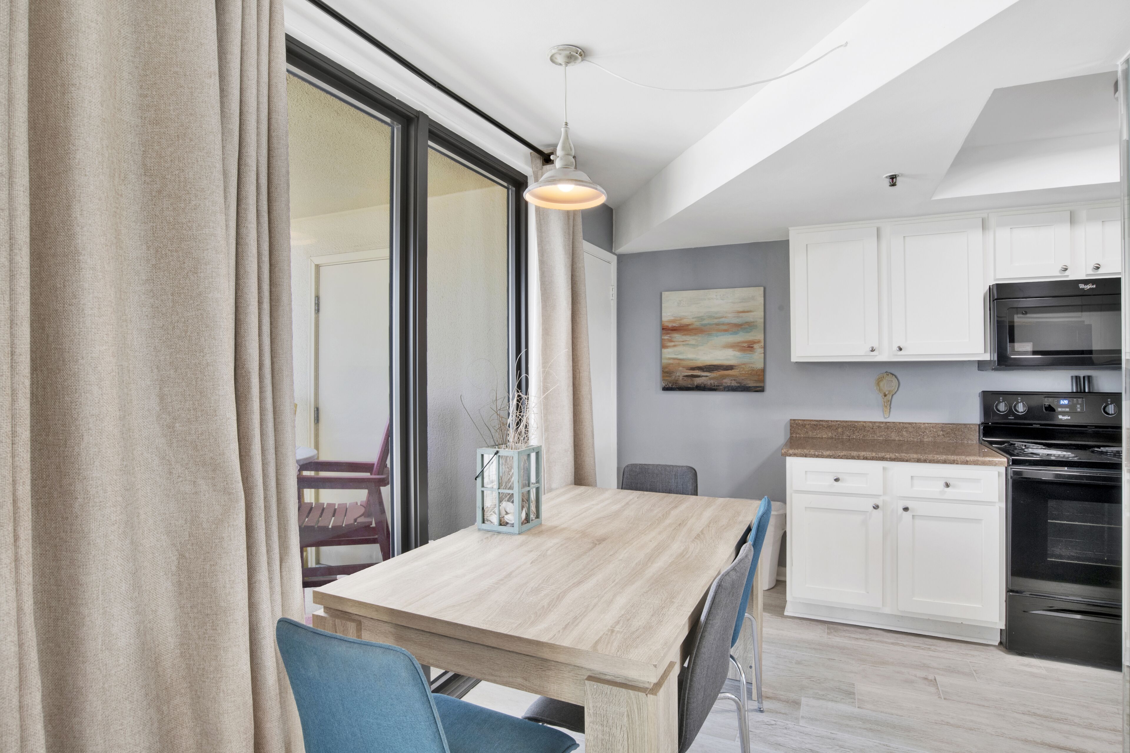 A modern kitchen with white cabinets, a wooden dining table, and a hanging light fixture.