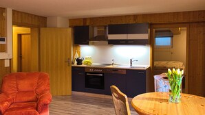 Una cocina compacta con paneles de madera, una zona de comedor con mesa redonda y un sillón rojo.