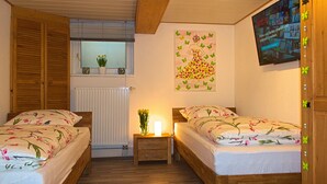 Un dormitorio con dos camas de madera, una ventana con persianas, un radiador, un televisor montado en la pared y un póster.
