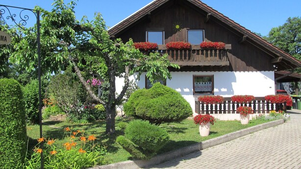 Una casa de madera tradicional con balcón, rodeada de jardines cuidados y un camino empedrado.
