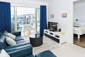 A modern living room with a leather sofa, a TV, and a balcony with blue curtains. - SEACRAZE D709 - 2 Bedroom - Near Beach (Tambon Nong Kae)