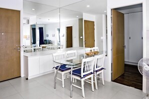 A modern dining area with a glass table and white chairs, a wooden door, and a white fan. - SEACRAZE D709 - 2 Bedroom - Near Beach (Tambon Nong Kae)