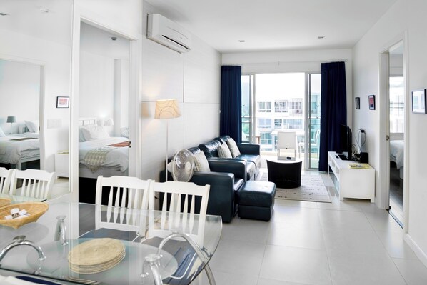 Une chambre d’hôtel moderne comprenant un coin repas, un salon avec un canapé et une télévision, ainsi qu’un balcon offrant une vue sur la ville.