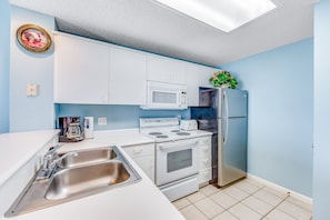 Compact kitchen with a stainless steel sink, stove, and refrigerator, featuring a clean layout and a small window.