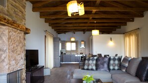 A living room with a stone fireplace, a sofa, a coffee table with a vase, and a kitchen in the background.