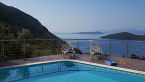 A swimming pool with two lounge chairs and a towel, overlooking a scenic view of the sea and hills.