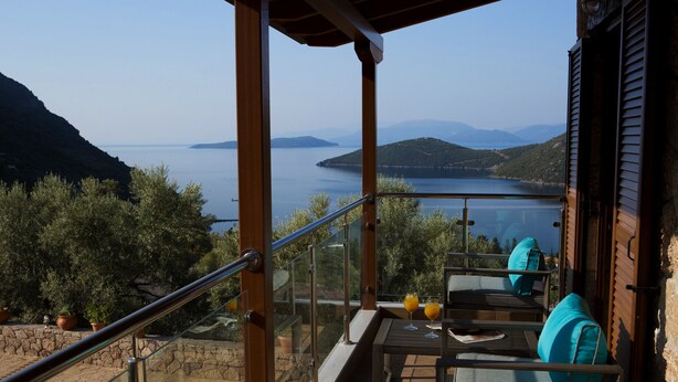 A balcony with a table and chairs, overlooking a lake and hills.