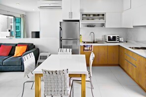 Eine moderne Küche mit weißen Schränken, einem Edelstahl-Kühlschrank, einer Mikrowelle und einem Essbereich mit einem weißen Tisch und Stühlen.