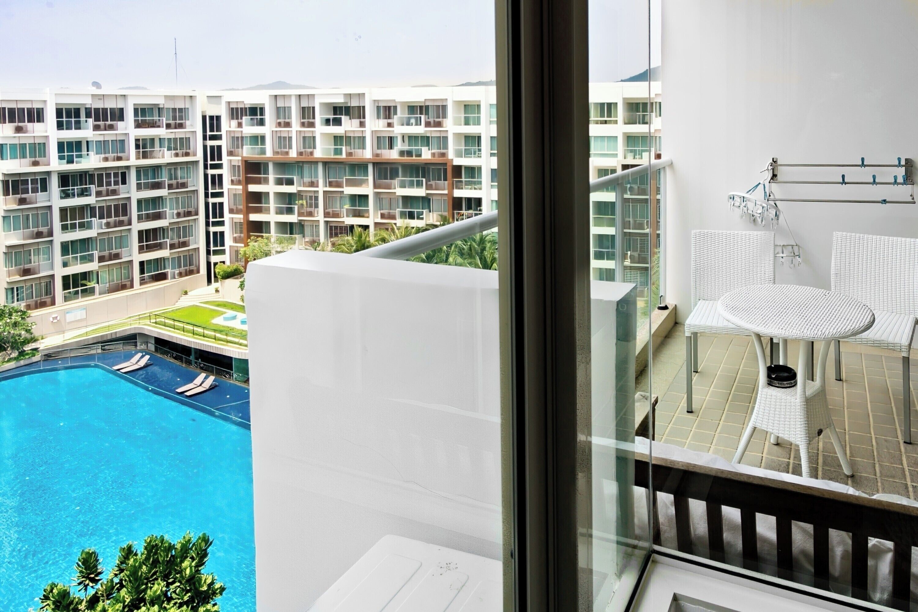 Une chambre d’hôtel moderne avec un balcon donnant sur une piscine et les bâtiments adjacents.