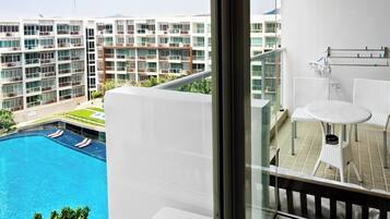 Une chambre d’hôtel moderne avec un balcon donnant sur une piscine et les bâtiments adjacents.