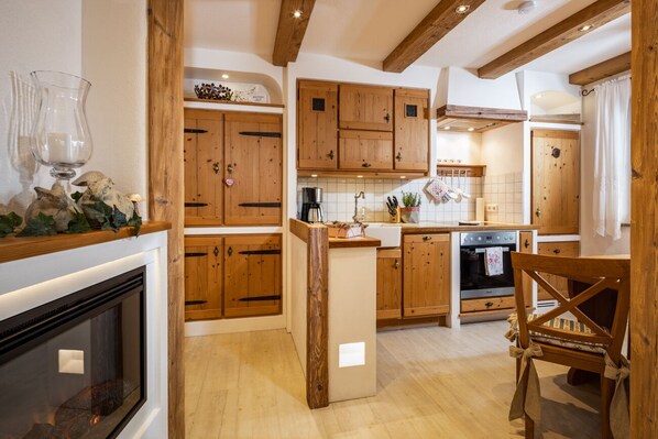 A kitchen with wooden cabinets, a central island, a stove, and a dining area with a chair.