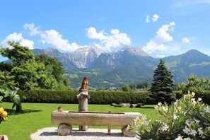 Une statue posée sur un banc en bois, avec une chaîne de montagnes en arrière-plan.