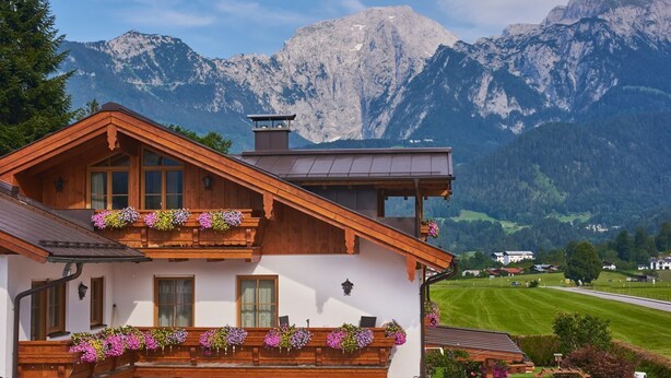 Eine traditionelle Holzhütte mit Balkonen, die mit Blumen geschmückt sind, vor einer Bergkulisse.