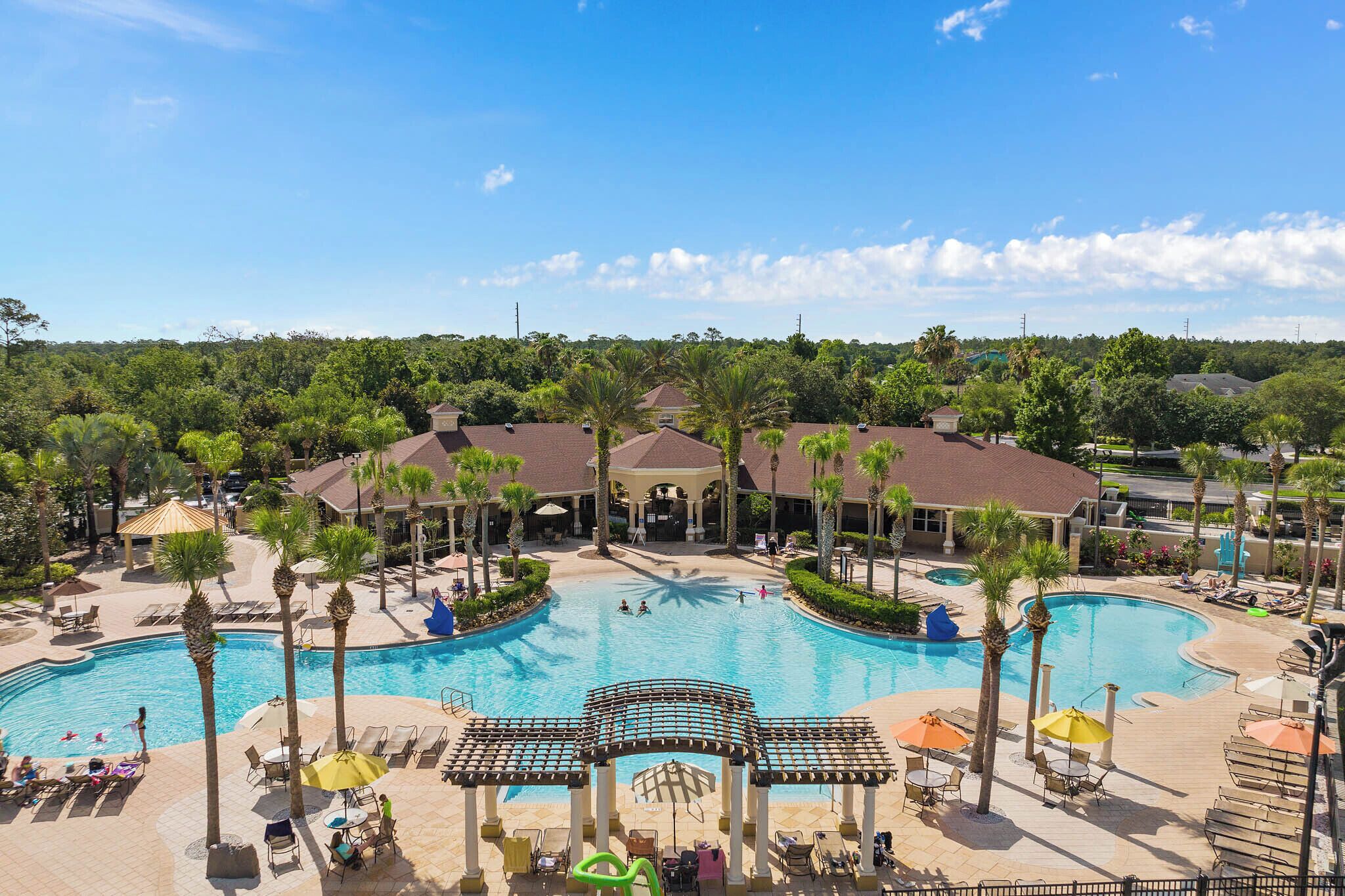 A resort with a large central pool, palm trees, and a covered area with seating.