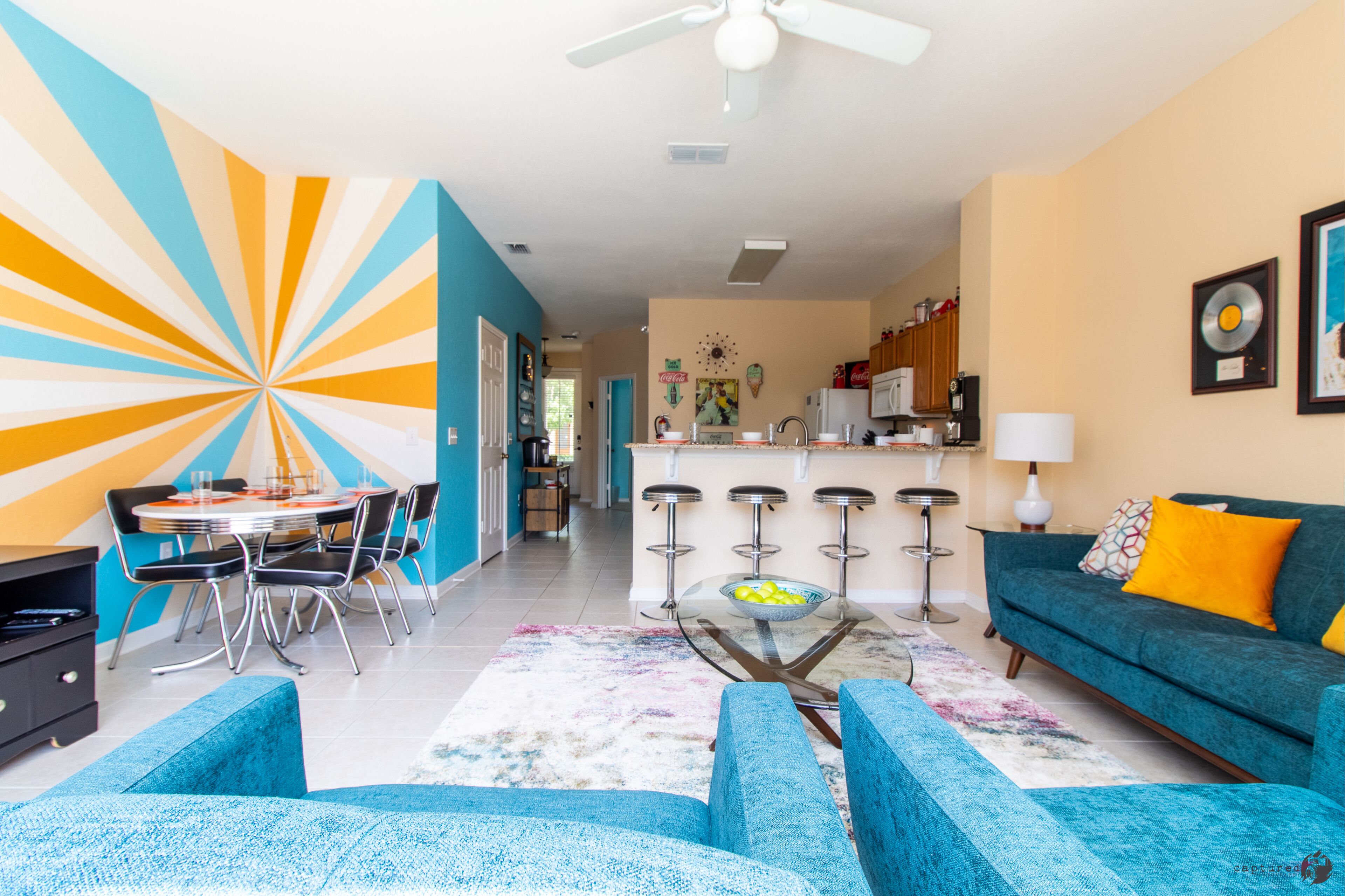 A modern living room with a blue sofa, a dining area with a round table, and a kitchen in the background.