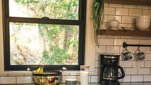 Una cocina con ventana, cafetera y frutero.