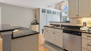 Una cocina moderna con una isla central, electrodomésticos integrados y un ventanal con persianas.