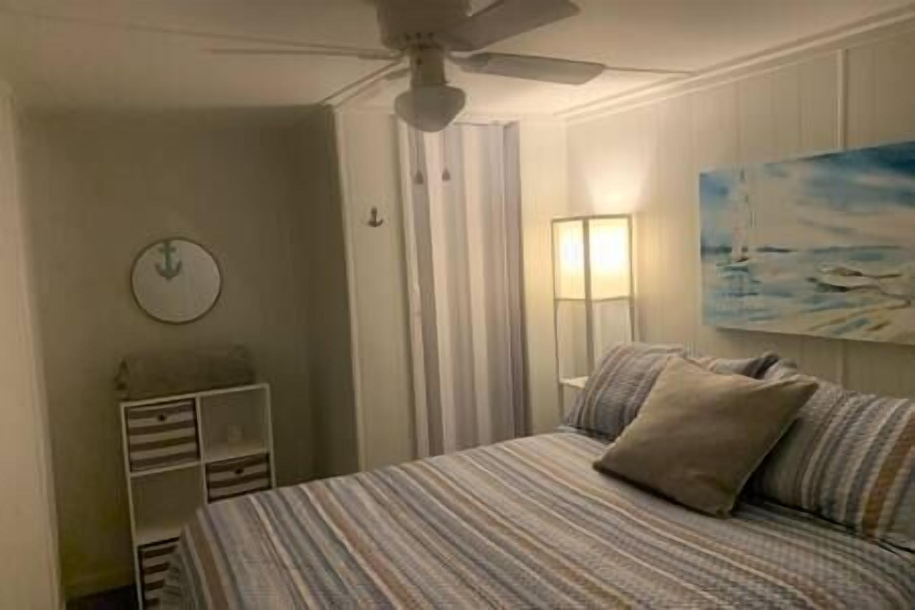 A bedroom with a bed, a ceiling fan, a nightstand, a lamp, and a painting on the wall.