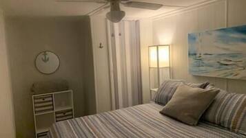 A bedroom with a bed, a ceiling fan, a nightstand, a lamp, and a painting on the wall.