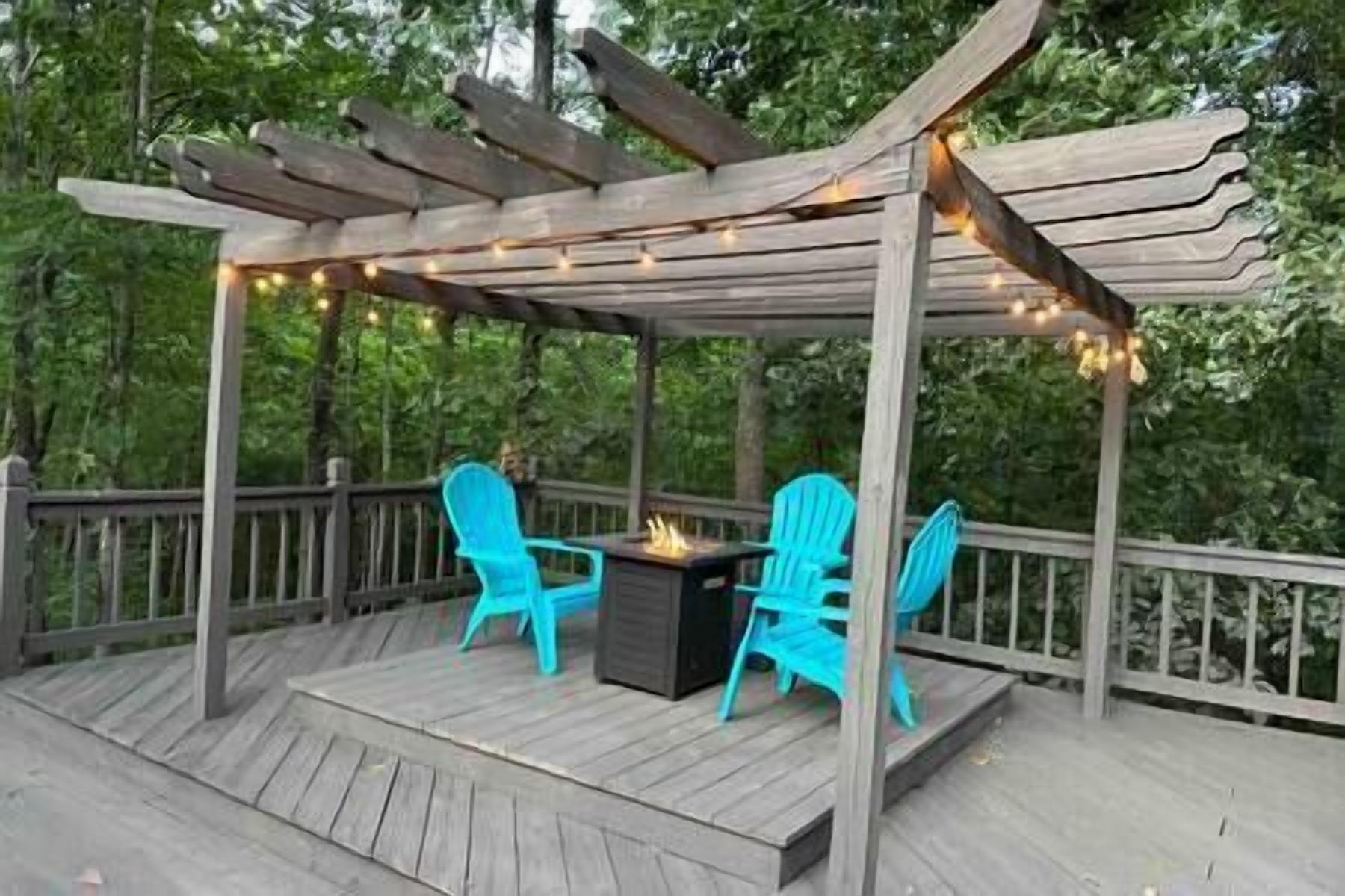 A wooden deck with a pergola, two blue chairs, and a fire pit.