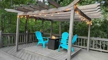 A wooden deck with a pergola, two blue chairs, and a fire pit.
