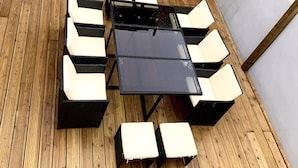 Una terraza de madera con una mesa negra y sillas blancas acolchadas.