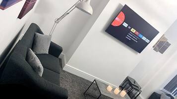 Een moderne woonkamer met een donkergrijze bank, een vloerlamp, een salontafel en een flatscreen-tv aan de muur, waarop verschillende streamingdiensten worden getoond.