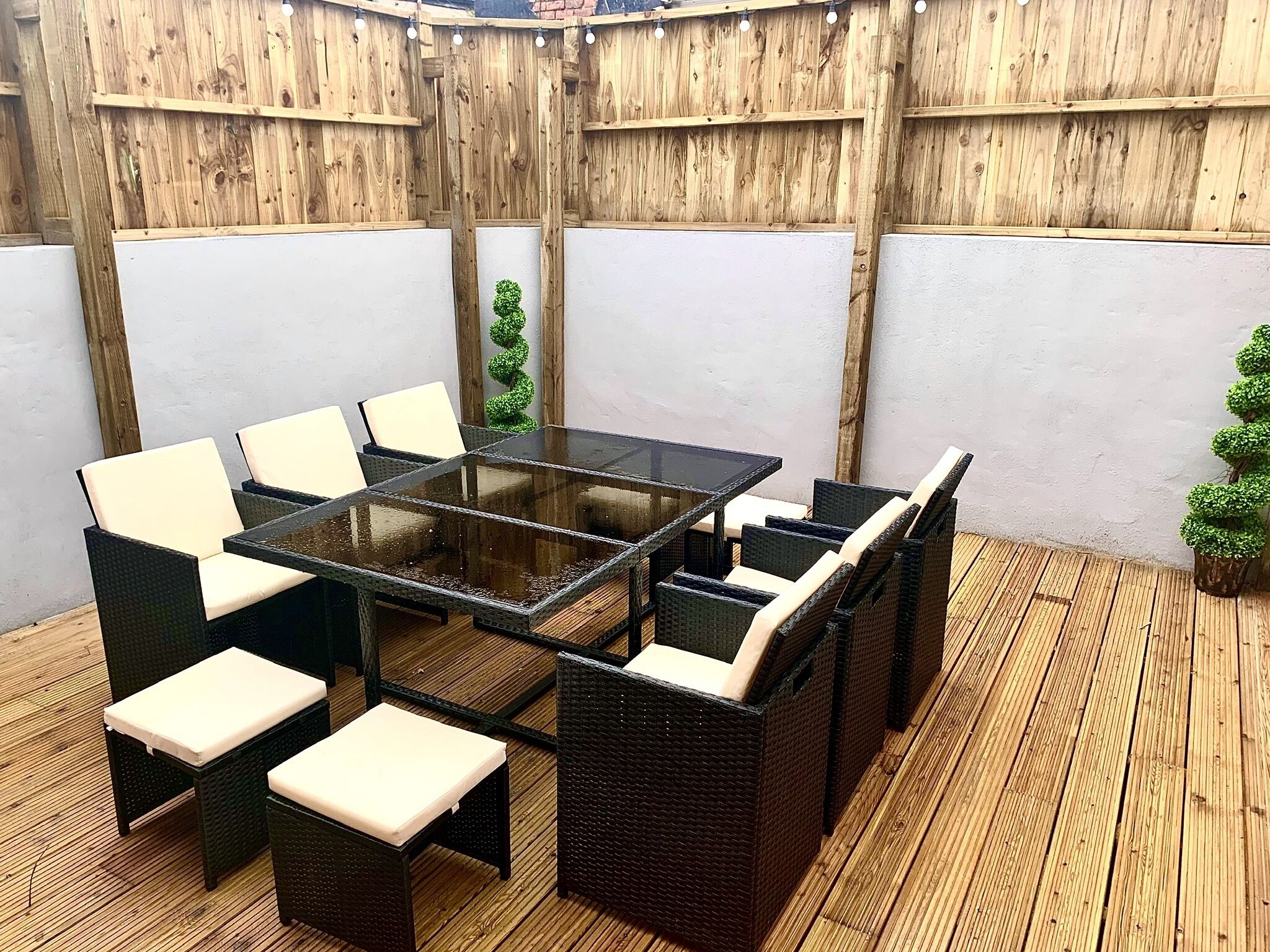 Un patio exterior con una mesa de vidrio rodeada de sillas de mimbre con cojines.