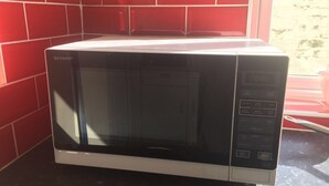 Un forno a microonde con display digitale e pannello di controllo, posizionato su un piano di lavoro scuro in una stanza con pareti in piastrelle rosse.
