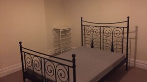 Un letto con struttura in metallo e un materasso semplice in una stanza dalle pareti spoglie e con pavimento rivestito di moquette.