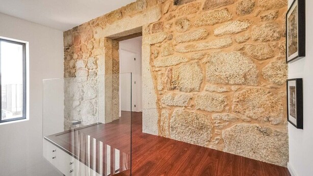 Un interior moderno con pared de piedra, barandilla de vidrio y suelo de madera.