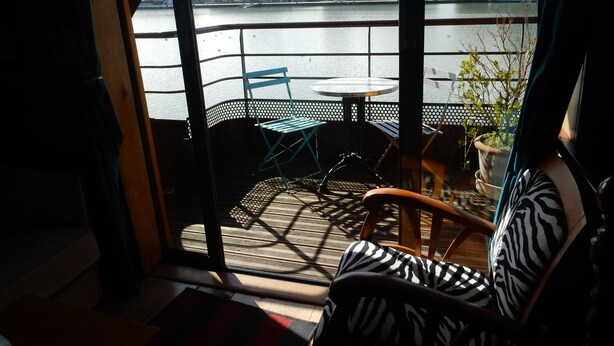 Une chambre avec vue sur une rivière, un balcon avec une table et des chaises, et un fauteuil à motifs zébrés.