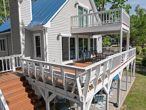 Une maison à deux étages dotée d’une terrasse en bois, d’un balcon et d’un espace extérieur aménagé et abrité.