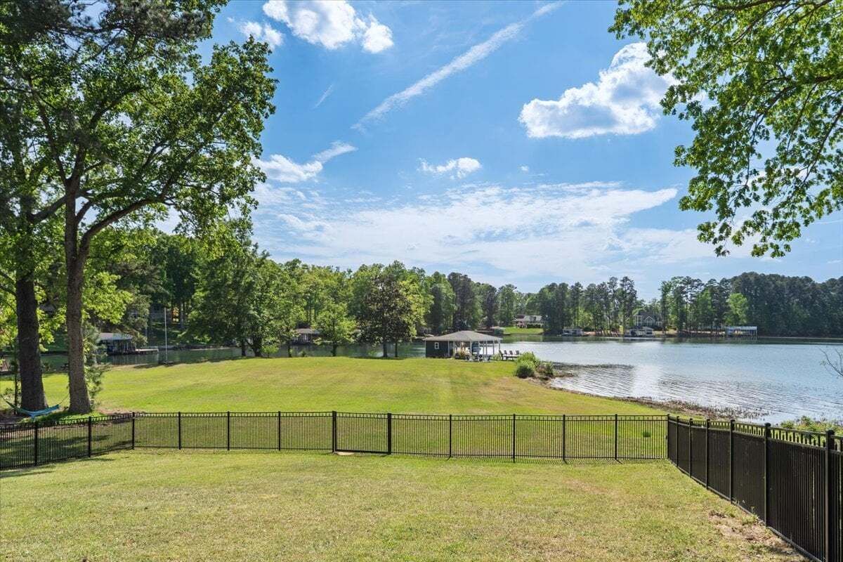 A fenced grassy area with a lake, trees, and a small pavilion.