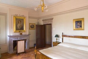 A bedroom with a bed, a fireplace, a door, and a chandelier.