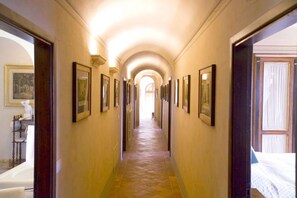 A hallway with framed pictures on the walls, leading to a room with a bed.