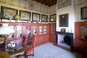 Una habitación con chimenea, estanterías, un globo terráqueo y cuadros en la pared.