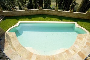 A swimming pool with a curved edge, surrounded by a stone wall and a grassy area.