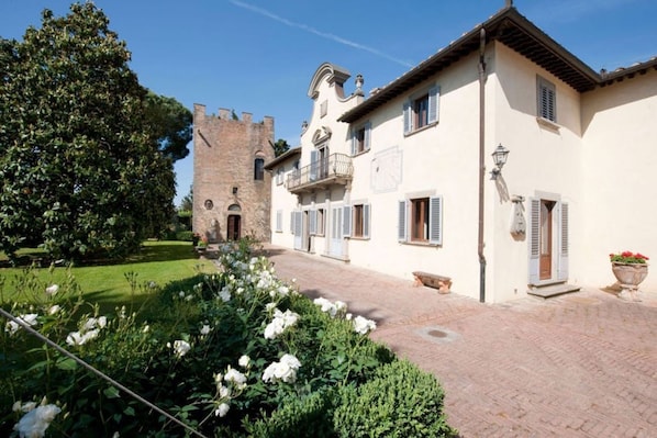 Un patio con una estructura similar a un castillo, un edificio con balcón y un jardín con flores blancas.
