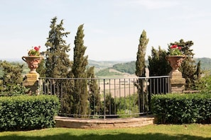 Un jardín cercado con árboles altos y vistas a un valle.