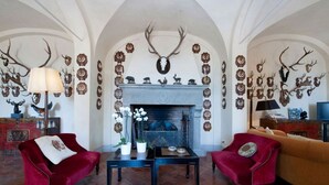 A room with a fireplace, two red armchairs, a sofa, and a table with decorative items. - Medieval castle turns into a Pool Villa and hosts Julia Roberts too. (Castelfiorentino)