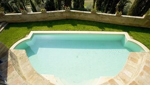A swimming pool with a curved edge, surrounded by a stone wall and a grassy area. - Medieval castle turns into a Pool Villa and hosts Julia Roberts too. (Castelfiorentino)