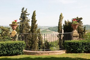 Un jardín cercado con árboles altos y vistas a un valle.