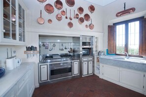 Una cocina con armarios blancos, electrodomésticos de acero inoxidable y utensilios de cobre en la pared.