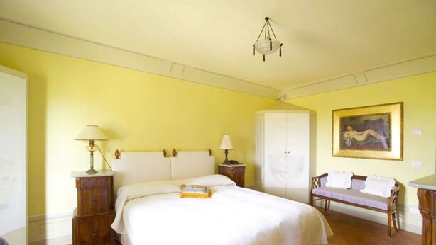 A bedroom with a large bed, two bedside tables with lamps, a wardrobe, a bench, and a painting on the wall. - Medieval castle turns into a Pool Villa and hosts Julia Roberts too. (Castelfiorentino)