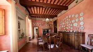 A dining room with a wooden table and chairs, a chandelier, and a wall decorated with plates. - Medieval castle turns into a Pool Villa and hosts Julia Roberts too. (Castelfiorentino)
