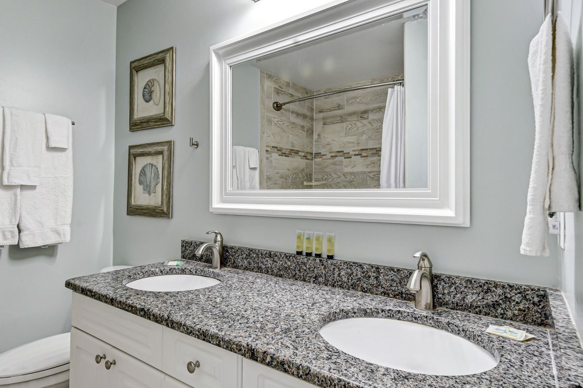 A bathroom with two sinks, a large mirror, and framed artwork on the wall.