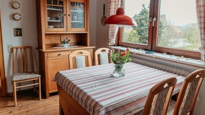 Un comedor con un mueble de madera, una mesa con mantel a rayas y un jarrón con flores.