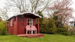 Una pequeña cabaña roja de madera con un porche y dos sillas a rayas.